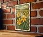 A framed illustration of a field of yellow daffodils is displayed on a brick wall.