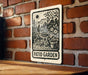 A sign for a patio garden is hanging on a brick wall.