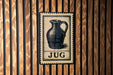 A metal sign with a vintage-style illustration of a jug is mounted on a wooden wall.