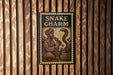 a sign with the text "SNAKE CHARM" and an illustration of a man with a snake.