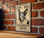 A vintage-style metal sign featuring a black and white illustration of a Teddy Roosevelt Terrier dog, mounted on a brick wall.