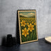 A framed illustration of a field of yellow daffodils is displayed on a gray wall, with a white plate and black camera lenses visible to the side.