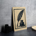 a wooden sign with a black and white illustration of a quill pen and inkwell, placed on a gray surface next to some black camera lenses.
