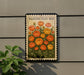 a framed illustration of a flower bed with orange and yellow flowers, mounted on a wall.