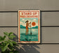 A sign that says "STAND UP PADDLEBOARDING" with an illustration of a woman paddleboarding on a lake.