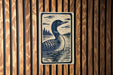 A wooden wall with a framed illustration of a loon, a type of bird, depicted in a black and white style.