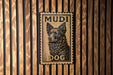 A metal sign with a dog's face on it, mounted on a wooden wall.