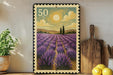 A framed stamp-like artwork depicting a field of lavender flowers with a sun and clouds in the background, placed on a shelf next to a wooden cutting board and a potted plant.