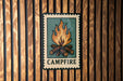 A metal sign with a campfire illustration is mounted on a wooden wall.