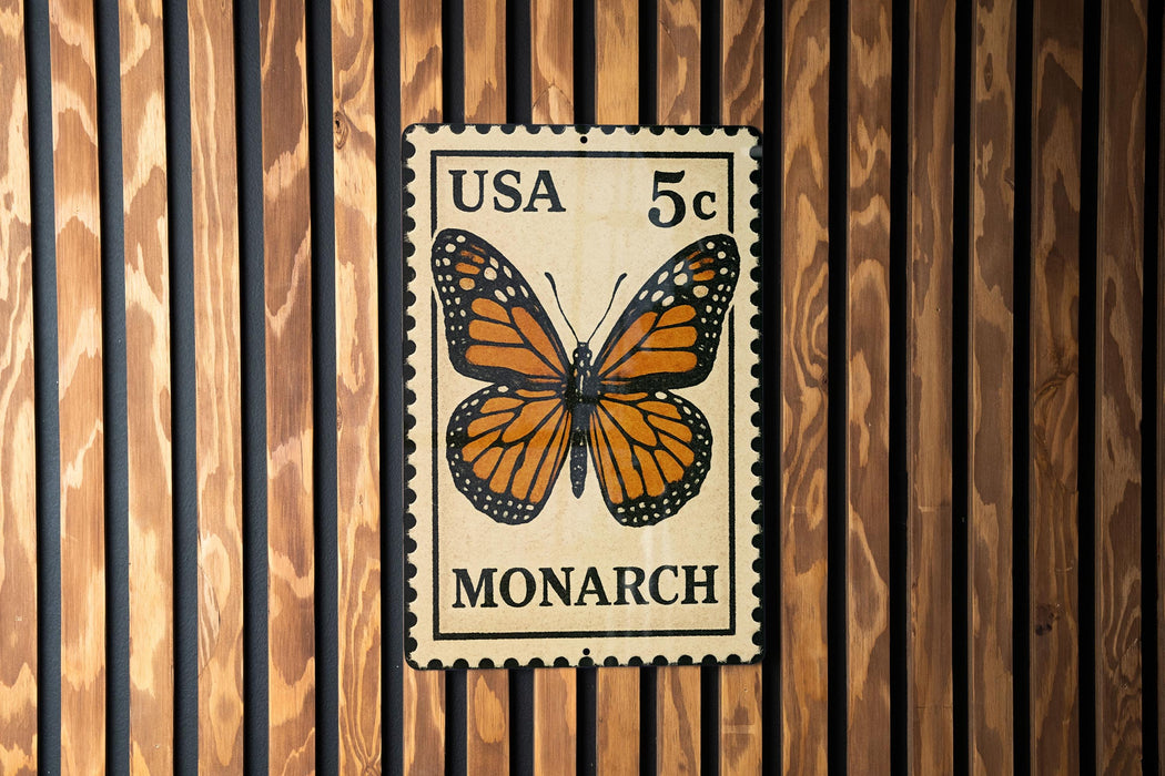 A US 5c postage stamp featuring a detailed illustration of a monarch butterfly is displayed on a wooden wall.