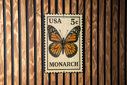 A US 5c postage stamp featuring a detailed illustration of a monarch butterfly is displayed on a wooden wall.