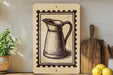a wooden shelf with various kitchen items, including a potted plant, a wooden cutting board, and a lemon. There is also a framed illustration of a pitcher on the shelf.