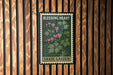 A framed poster of a plant with pink flowers is displayed on a wooden wall.
