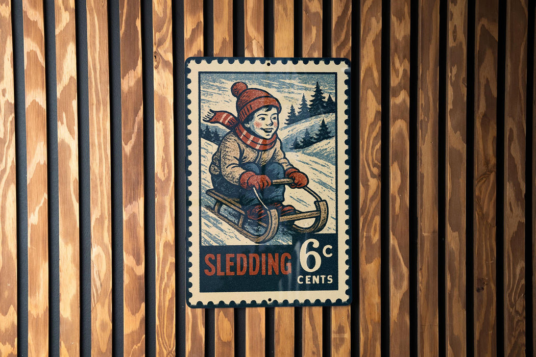 A vintage-style postage stamp depicting a young boy riding a sled, with the text "Sledding 6c" and a snowy landscape in the background.