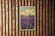 A postage stamp depicting a field of lavender flowers, with a sun and clouds in the background.