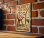 A vintage-style sign with the text "TARGET PRACTICE" and an illustration of a target with arrows is displayed on a brick wall.