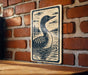 A wooden table with a decorative sign featuring a black and white illustration of a bird, likely a duck, swimming in a body of water.