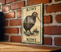 A framed illustration of a kiwi bird is displayed on a brick wall, with the word "KIWI" written on the frame.