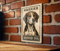 A vintage-style metal sign featuring a portrait of a Harrier dog is mounted on a brick wall.