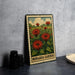 A metal sign with a floral illustration of red flowers and green leaves, placed on a table next to some black camera lenses.