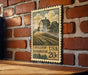 A vintage-style stamp depicting a farmhouse is mounted on a brick wall.
