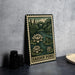 A metal sign with a garden pond illustration, featuring a frog and water lilies, is displayed on a table next to some black camera lenses.