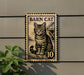 A sign featuring a cat illustration, mounted on a wall next to a plant.