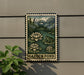 A metal sign with a painting of a garden pond and a frog, mounted on a wall next to a plant.