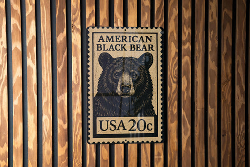 A black and white stamp-like sign with an illustration of a black bear on it, mounted on a wooden wall.