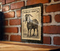 A metal stamp featuring a detailed illustration of a goat, mounted on a brick wall.