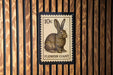 A 10c postage stamp featuring a rabbit illustration, mounted on a wooden wall.