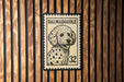 A Dalmatian dog is depicted on a postage stamp, which is mounted on a wooden wall.