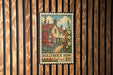 A vintage-style postage stamp featuring a house surrounded by flowers, hanging on a wooden wall.