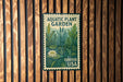A metal sign with a lush green plant illustration and a white water lily, mounted on a wooden wall.