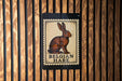A sign featuring a picture of a brown hare, with the text "Belgian Hare" below it, mounted on a wooden wall.