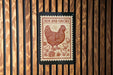 A wooden wall with a framed image of a chicken, which appears to be a stamp or a sign with the text "HEN AND CHICKS".