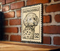 A Dalmatian dog is depicted on a postage stamp-like sign, which is mounted on a brick wall.