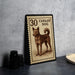 A framed stamp depicting a dog, with the text "30 CANAAN DOG" printed on it, is displayed on a table next to some black camera lenses.