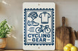 a sign that reads "CYCLING GEAR" with various cycling-related icons, such as a helmet, a bicycle, and a pair of shoes. The sign is displayed on a shelf next to a potted plant and a wooden cutting board.