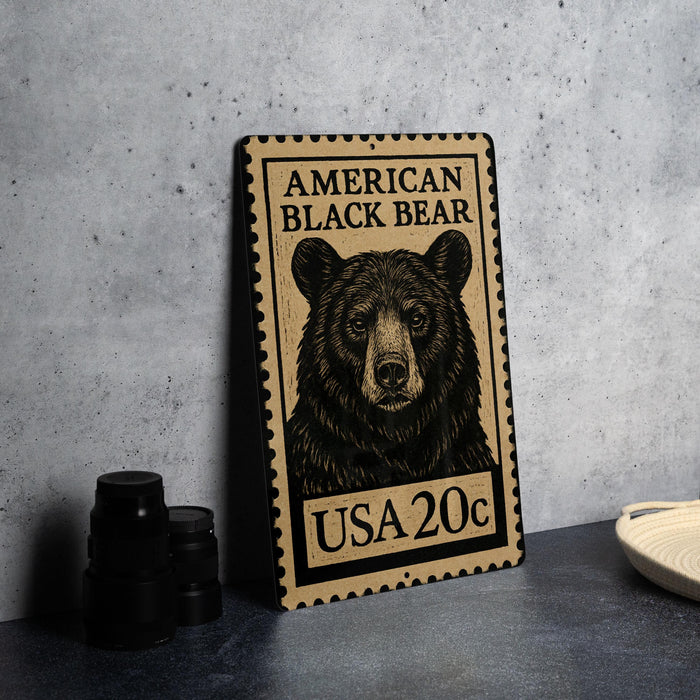 A metal sign featuring a black bear illustration and the text "AMERICAN BLACK BEAR" and "USA 20c" printed on it, placed on a gray countertop next to some black camera lenses.