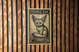 a close-up of a stamp or postcard with a fennec fox illustration on it, mounted on a wooden wall.