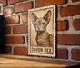 a wooden table with a framed picture of a Devon Rex cat on it, mounted on a brick wall.