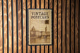 A vintage postage stamp with a cityscape illustration is displayed on a wooden wall.