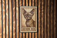 A metal stamp featuring a cat's portrait is displayed on a wooden wall.
