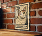 A wooden table with a wooden border, against a brick wall. There is a framed Turkish postage stamp featuring a cat on the table.