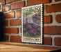 A US postage stamp featuring a field of purple flowers is displayed on a brick wall.