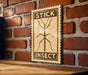 A wooden table with a brick wall in the background, and a framed sign with the word "STICK" and an illustration of a stick insect.