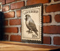 A metal sign with a postage stamp design featuring a parrot is mounted on a brick wall.