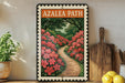 A framed poster of a garden path with red flowers is displayed on a shelf, accompanied by a wooden cutting board and a potted plant.
