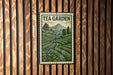 A metal sign with a green and white illustration of a tea garden, mounted on a wooden wall.